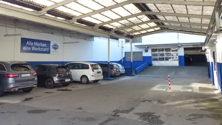 Hof der Autowerkstatt Wittmann mit Werkstatteinfahrt und dem Schriftzug „Alle Marken, eine Werkstatt“