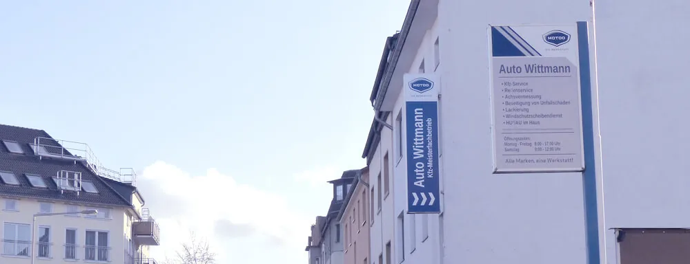Firmenschild von Auto Wittmann an der Hausfassade in Köln-Nippes mit Leistungsübersicht und Öffnungszeiten